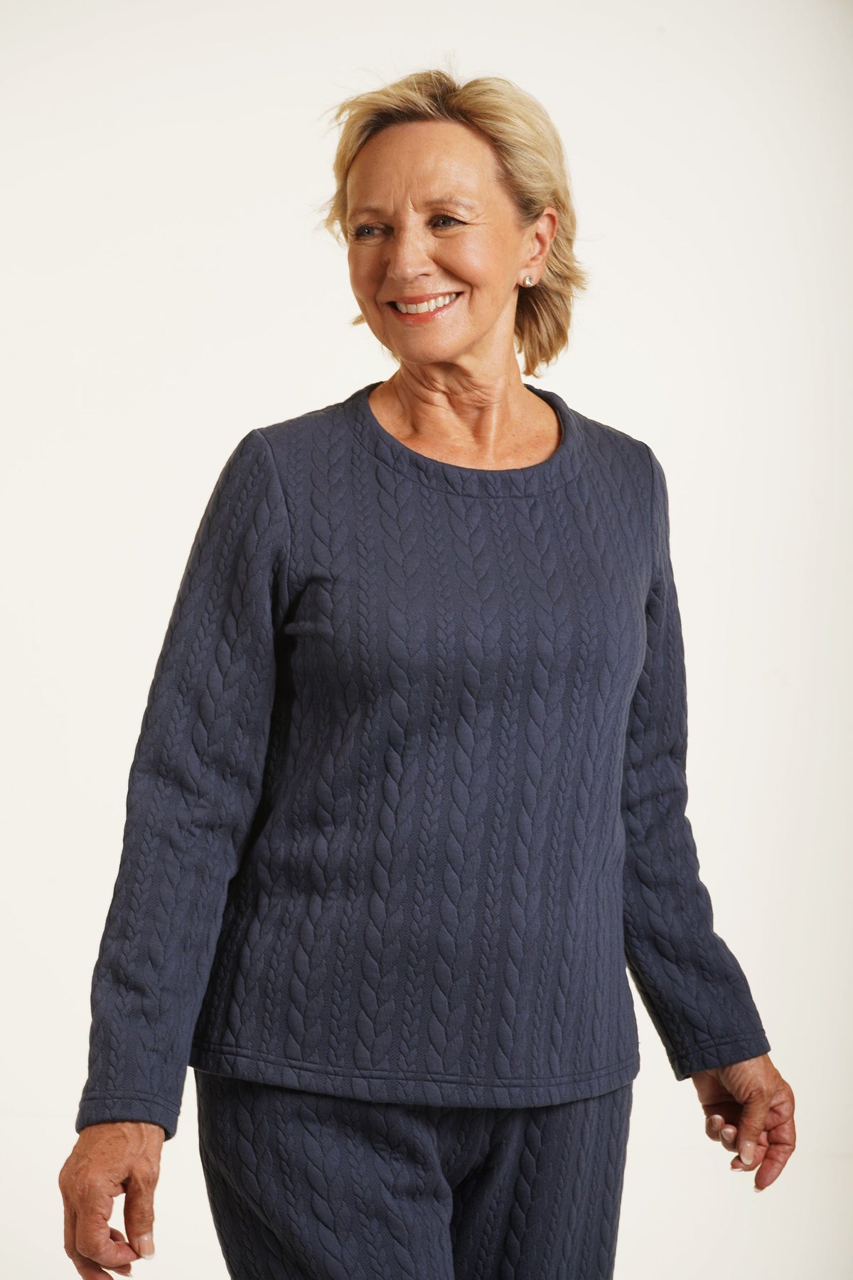 Woman wearing a navy long sleeve top with allover cable texture and a round neckline, with matching navy bottoms, against a plain light background._0