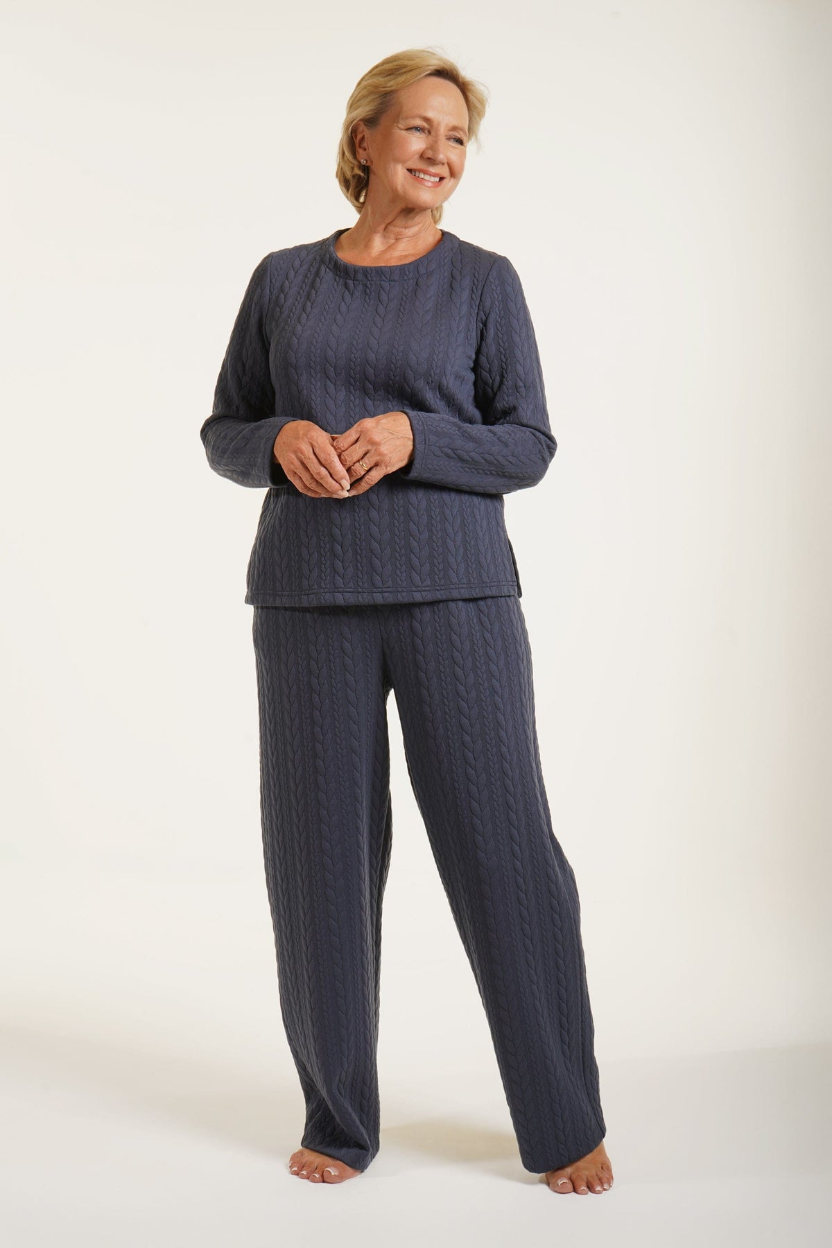 Woman wearing a navy long sleeve top with allover cable texture and a round neckline, with matching navy bottoms, against a plain light background._5