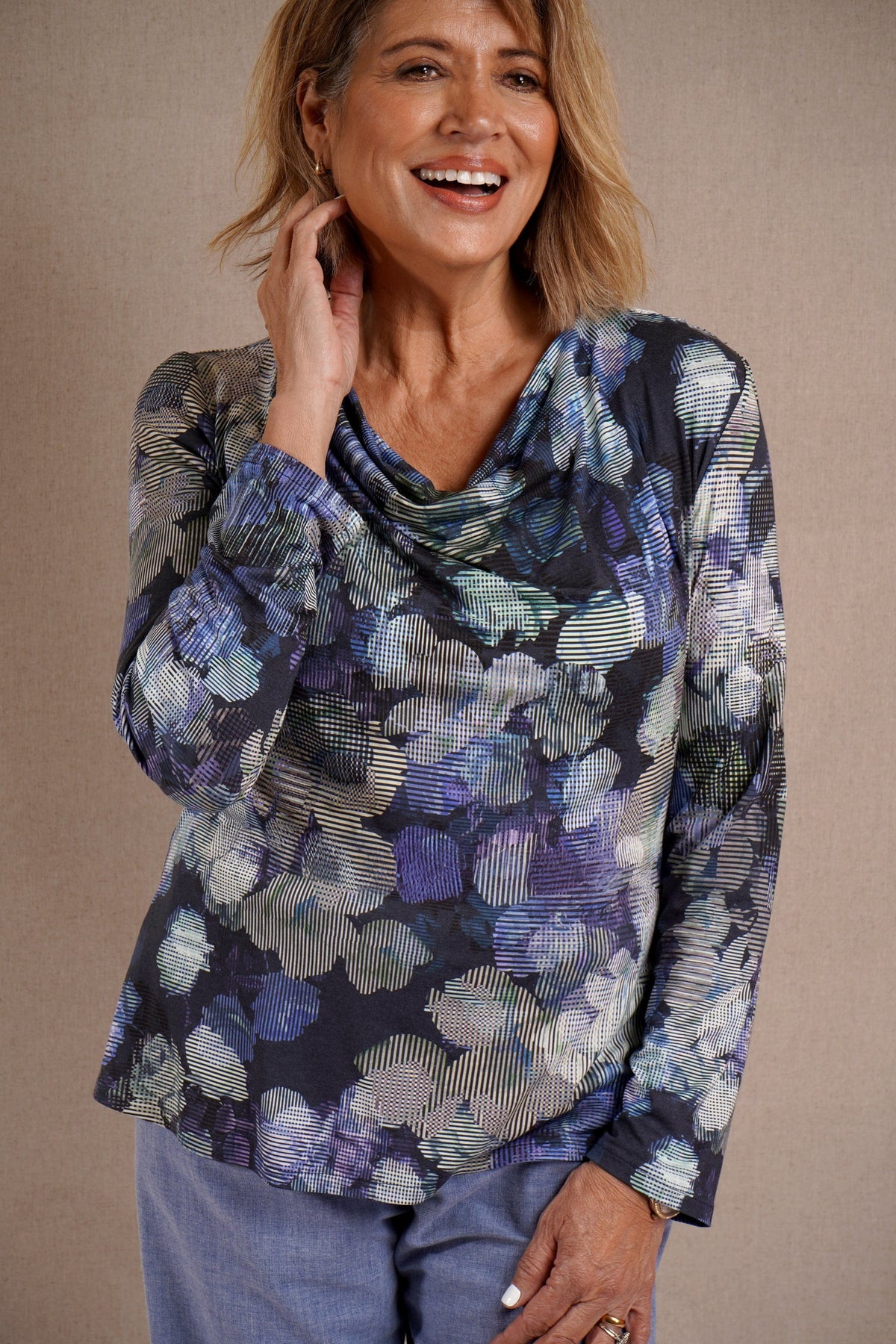 Woman wearing a long sleeve cowl neck top with an abstract navy, blue, lilac and cream print, paired with light blue trousers._0