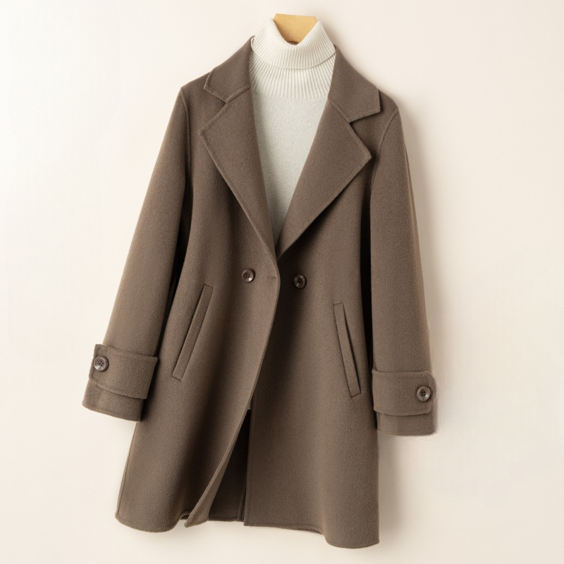 A tailored double breasted coat with notched lapels, front pockets, and buttoned cuff tabs displayed on a mannequin._0