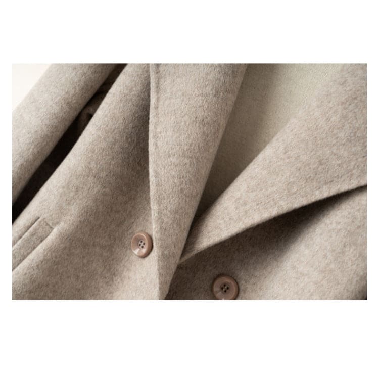 A tailored double breasted coat with notched lapels, front pockets, and buttoned cuff tabs displayed on a mannequin._10
