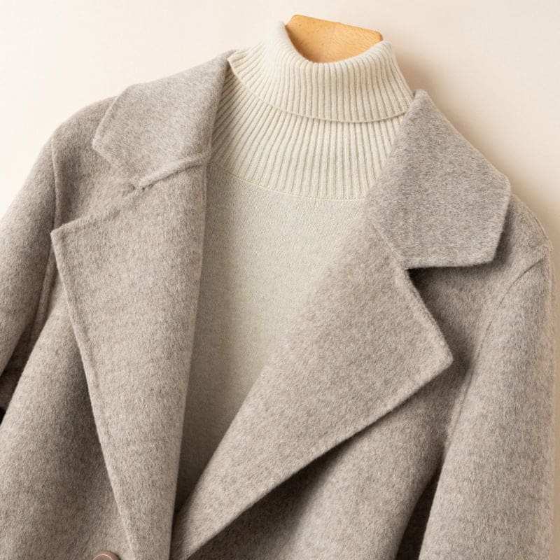 A tailored double breasted coat with notched lapels, front pockets, and buttoned cuff tabs displayed on a mannequin._11