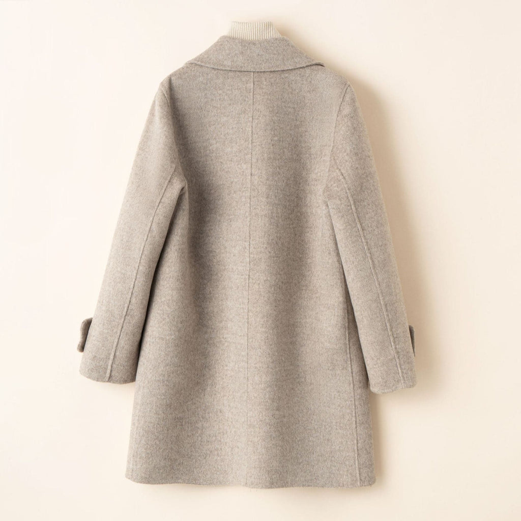A tailored double breasted coat with notched lapels, front pockets, and buttoned cuff tabs displayed on a mannequin._4