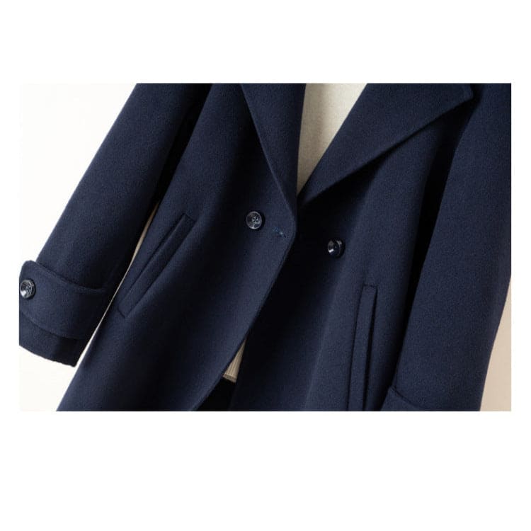 A tailored double breasted coat with notched lapels, front pockets, and buttoned cuff tabs displayed on a mannequin._8