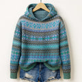 Hooded knit sweater with fair isle patterning in teal, green, lavender and grey, hanging on a wooden hanger above ripped denim shorts._0