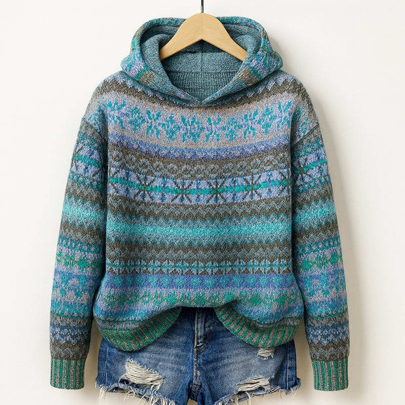 Hooded knit sweater with fair isle patterning in teal, green, lavender and grey, hanging on a wooden hanger above ripped denim shorts._0