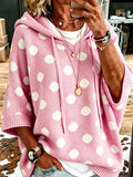 Person wearing a loose pink hooded knit pullover with white polka dots, drawstring ties and half sleeves over a white top and jeans._0