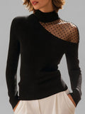 Woman wearing a fitted black ribbed turtleneck sweater with an asymmetric shoulder cutout covered in sheer black polka dot mesh, paired with cream trousers._0