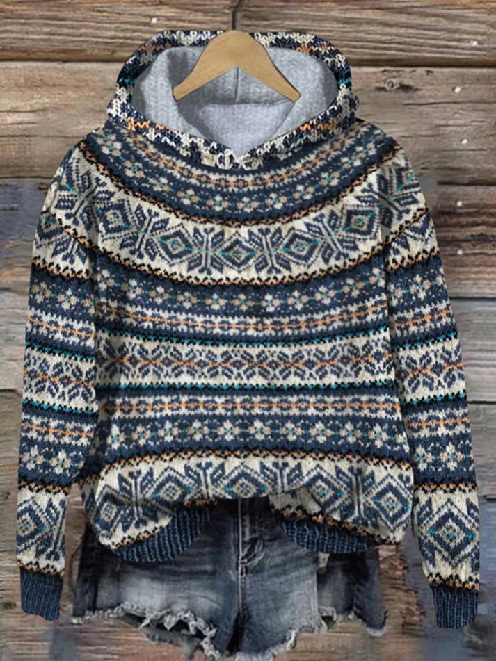 Nordic-pattern hooded sweater in navy, cream, and warm brown with long sleeves and ribbed cuffs, displayed on a hanger over distressed denim shorts.