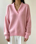 Woman wearing an oversized soft pink v-neck sweater with ribbed collar, cuffs and hem, paired with white trousers._0