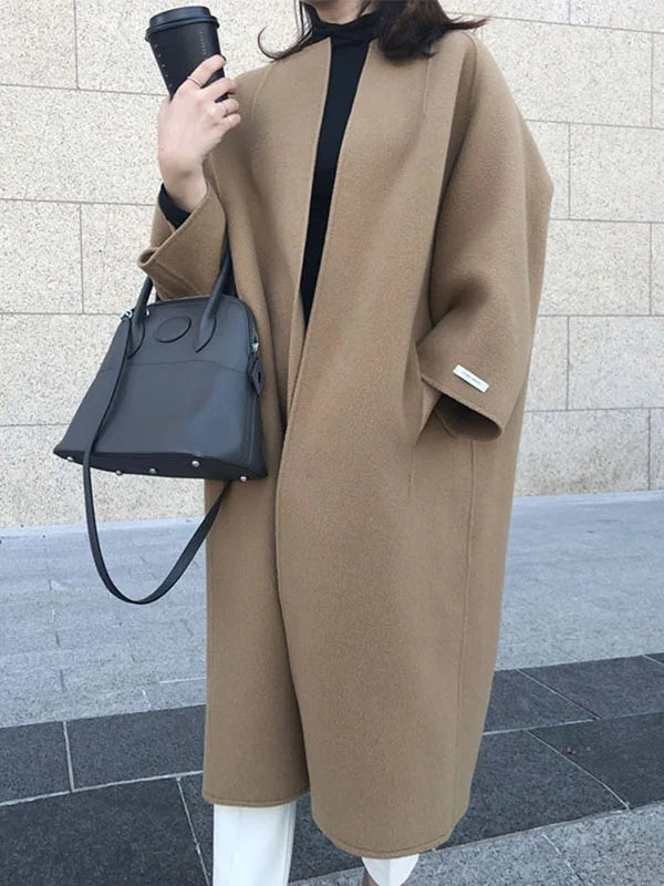 Camel open-front longline coat styled with a black top, white trousers, a black handbag, and a takeaway cup; bracelet-length sleeves are visible.