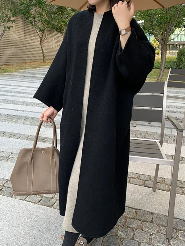 Black open-front coat shown in motion, emphasizing its flowing longline silhouette and wide bracelet sleeves over a light outfit.