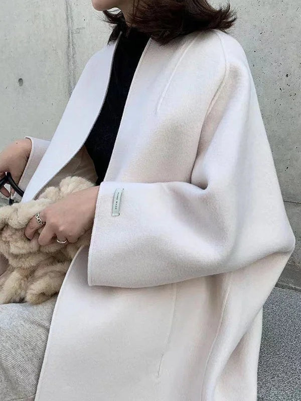 Close side view of the ivory coat showing the open front, smooth longline panel, and prominent bracelet-length sleeve.