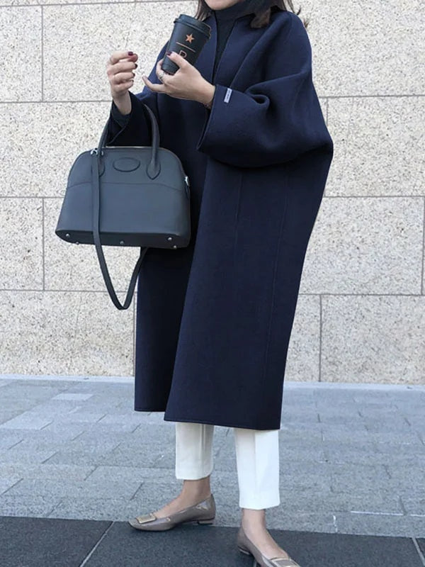 Three-quarter view of the navy open-front longline coat with bracelet sleeves, styled over white trousers and a dark handbag.