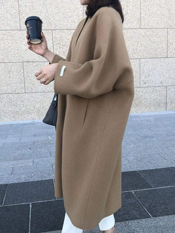 Side view of the camel longline coat showing its relaxed drape, open front, bracelet sleeves, and long vertical silhouette.