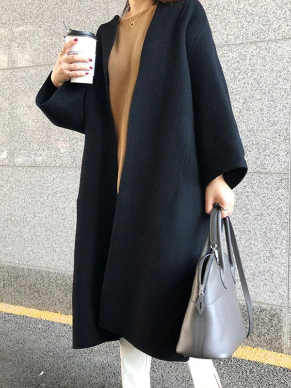 Front view of the black longline coat showing its clean open front, bracelet sleeves, and relaxed shape over a camel top.