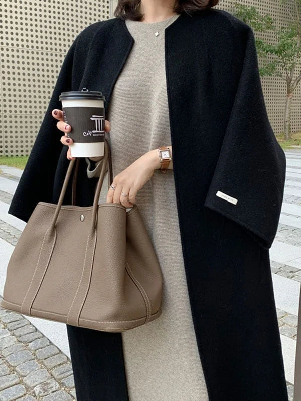 Close front view of the black open-front coat worn over a light dress, with a bracelet sleeve and sleeve label clearly visible.