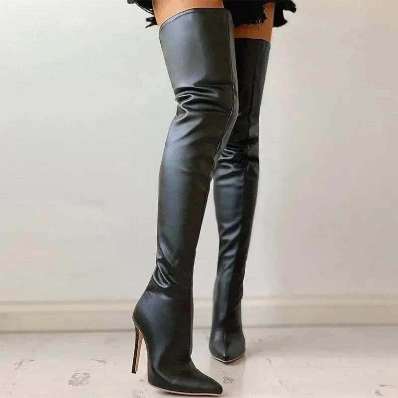 Angled view of black over-the-knee boots showing the pointed front, tall fitted shafts, and narrow heels while worn.