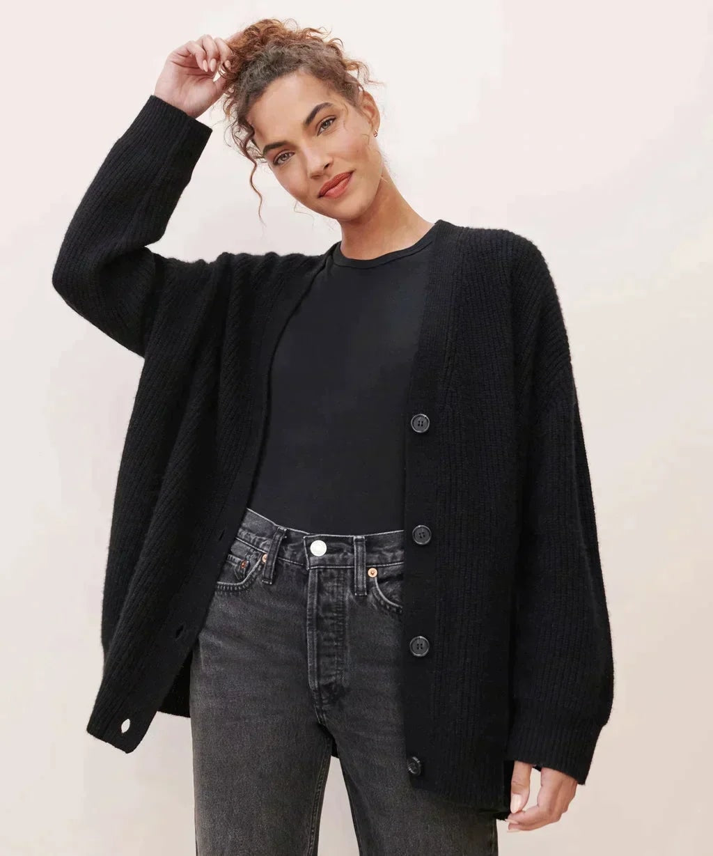 Black oversized V-neck button cardigan worn over a black top and gray jeans, shown with the relaxed sleeves and open front clearly visible.