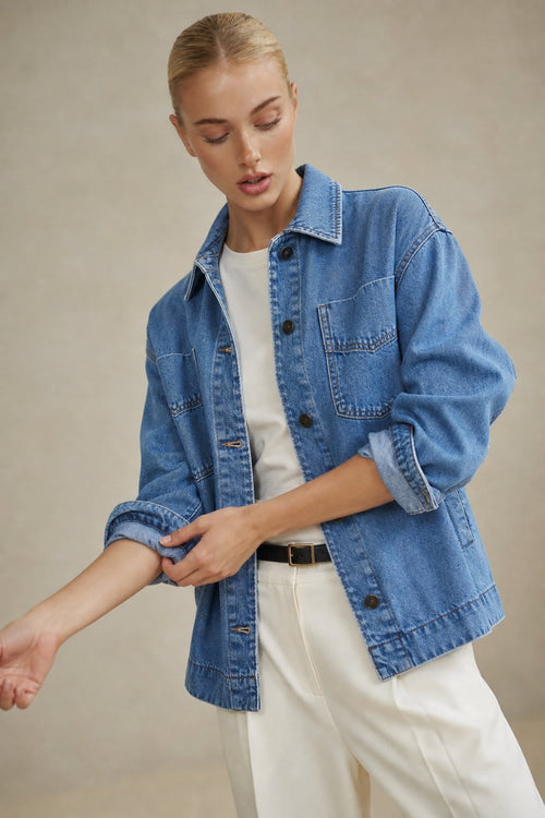 Woman wearing an oversized button-front jacket with chest pockets and a relaxed silhouette, styled over a white top and pants._0
