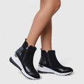 Woman wearing sporty platform ankle boots with textured panels, wedge sole, and side zipper closure._0
