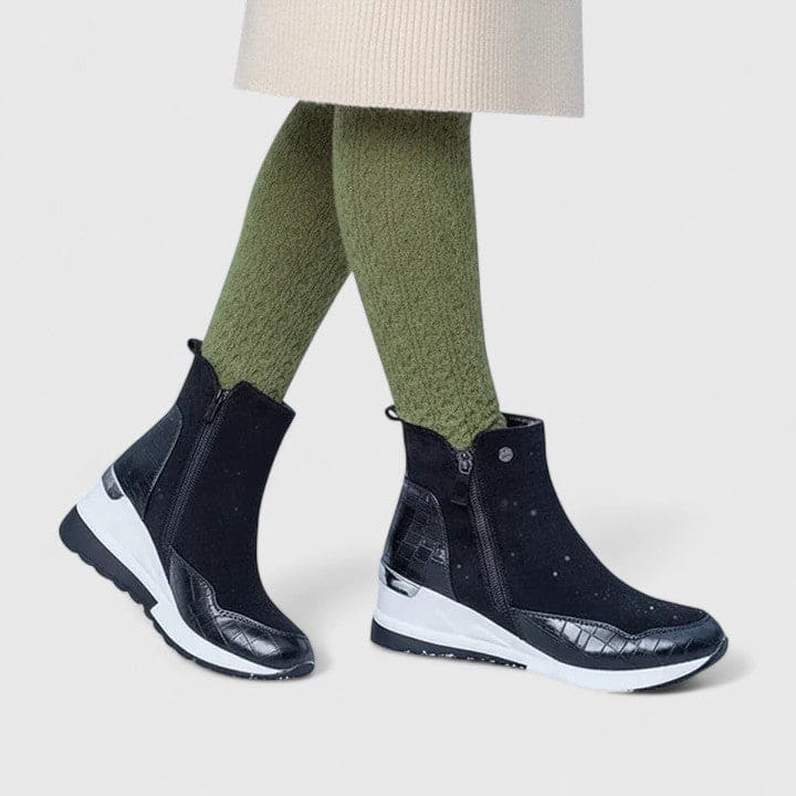 Woman wearing sporty platform ankle boots with textured panels, wedge sole, and side zipper closure._3