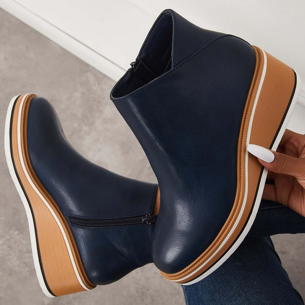 Navy blue ankle boot held above another boot to display the side zipper and full platform wedge.