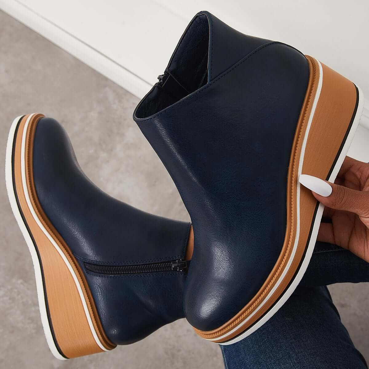 Navy blue ankle boot held above another boot to display the side zipper and full platform wedge.