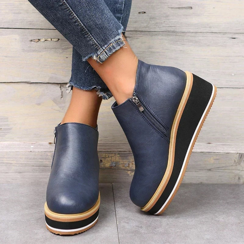 Navy blue ankle boots crossed against a wood backdrop, showing the zipper and contrasting sole layers.