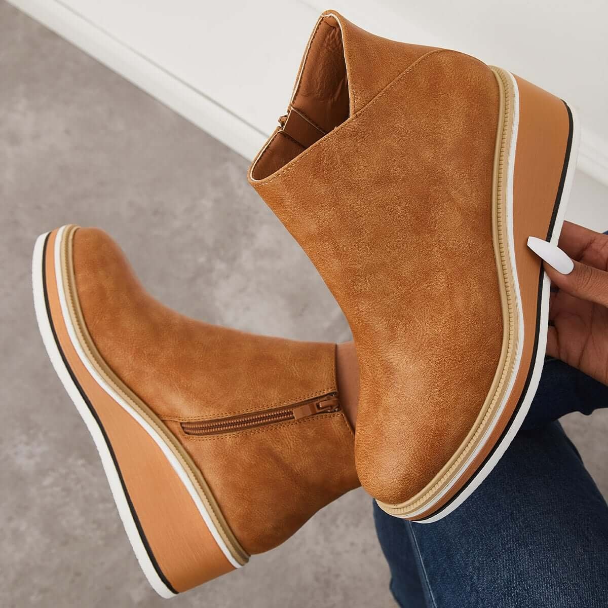 Tan ankle boot held above another boot to highlight the zipper, ankle opening, and platform profile.