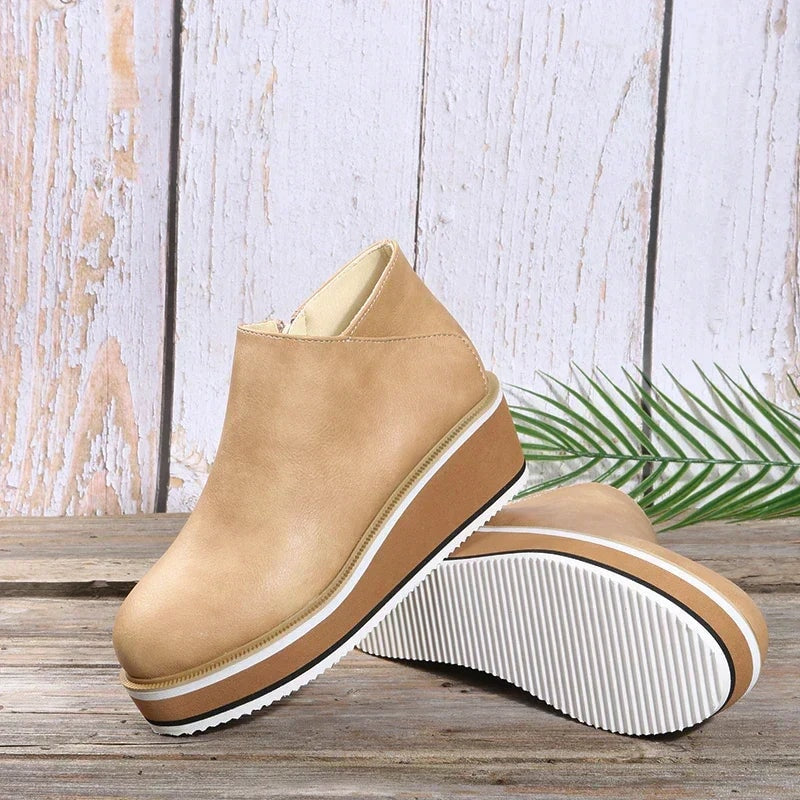 Light beige platform ankle boots arranged on a wooden surface, with one sole facing upward to show its ridged tread.