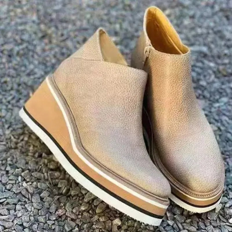 Light beige ankle boots displayed outdoors on gravel from a three-quarter angle, showing their raised platforms.