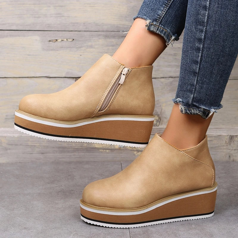 Light beige platform ankle boots shown in side view against wood, with the side zipper and textured outsole visible.