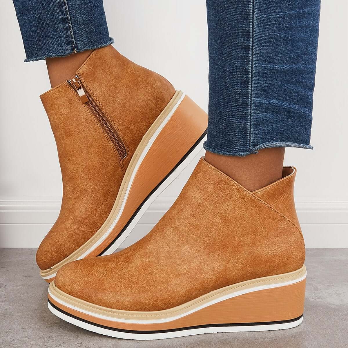 Tan platform ankle boots worn together in side view, with one boot angled upward to reveal the zipper.