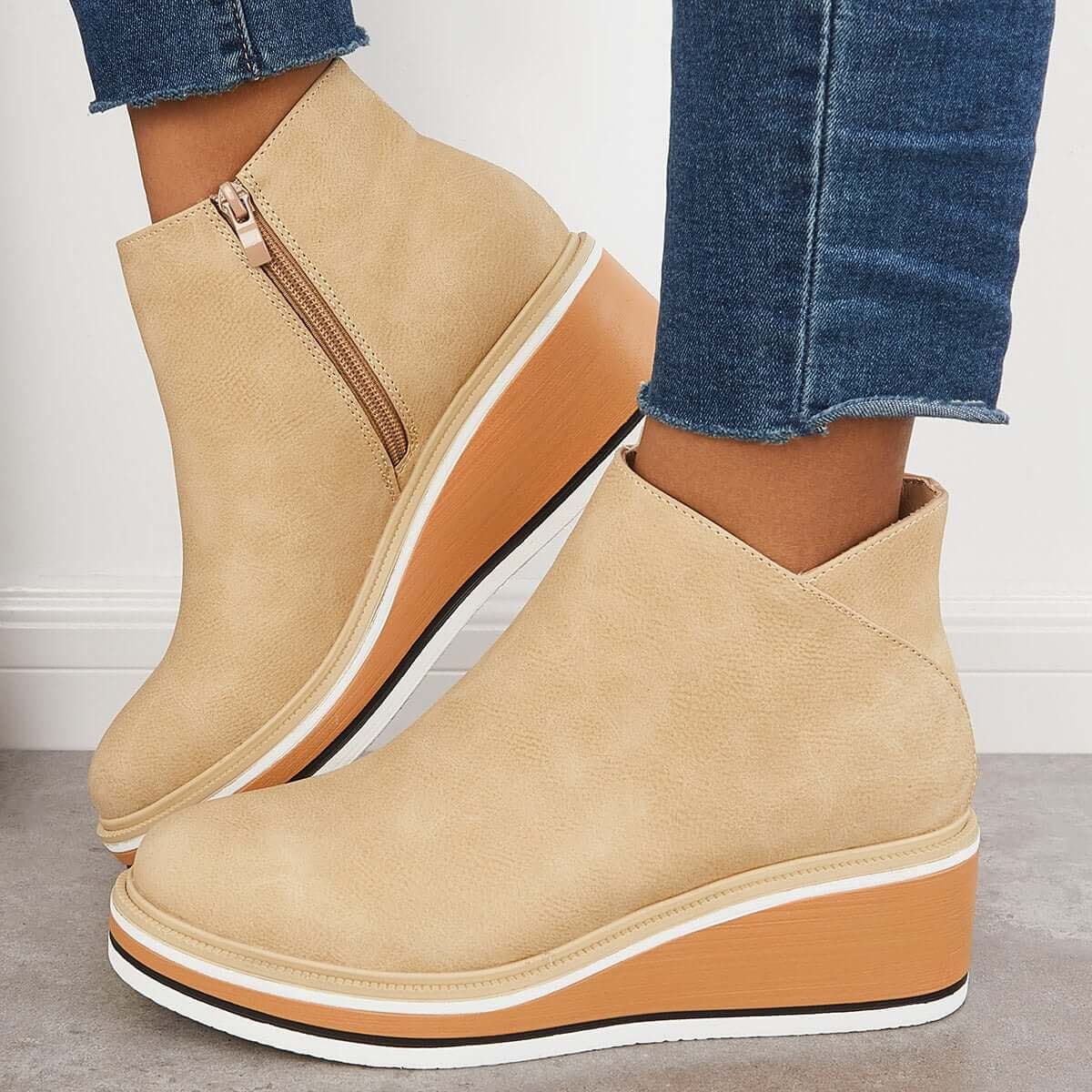 Light beige platform ankle boots worn with cropped jeans, showing the side zipper and wedge profile.