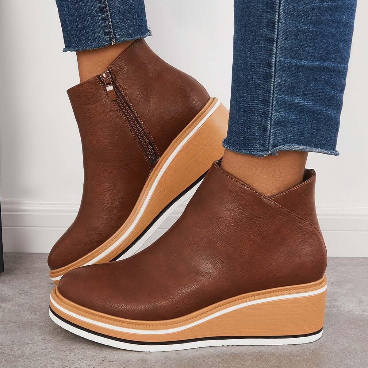 Brown platform ankle boots worn in side view, highlighting the side zipper, rounded toes, and raised sole.