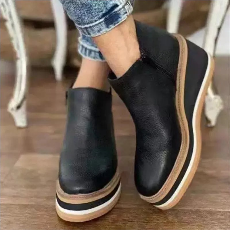 Black platform ankle boots posed with one foot angled inward, emphasizing the rounded front and layered sole.