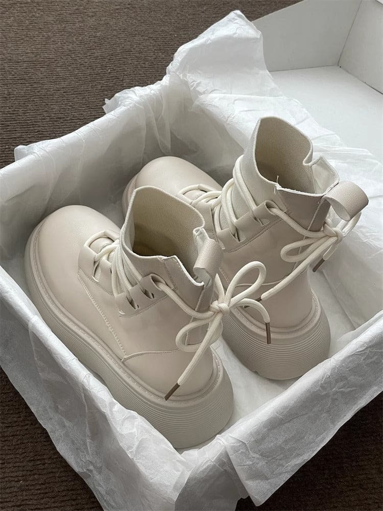 Pair of high-top lace-up platform boots with chunky soles in a neutral tone, displayed on white tissue paper in an open box._3