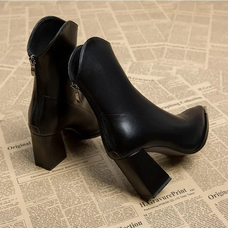 Black ankle boots positioned in a side profile, emphasizing the curved ankle shape, pointed front, side zipper, and block heel.
