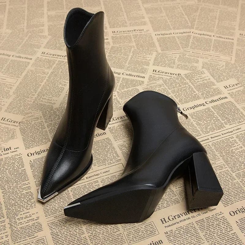 Pair of pointed toe chelsea boots with chrome tip detail and chunky block heel displayed on newspaper background_0