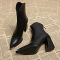 Pair of pointed toe chelsea boots with chrome tip detail and chunky block heel displayed on newspaper background_0