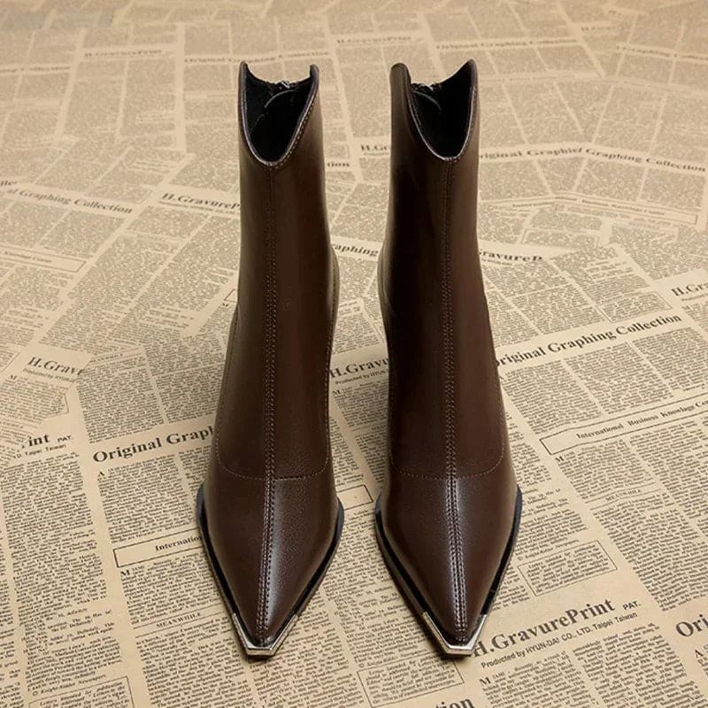 Pair of pointed toe chelsea boots with chrome tip detail and chunky block heel displayed on newspaper background_1
