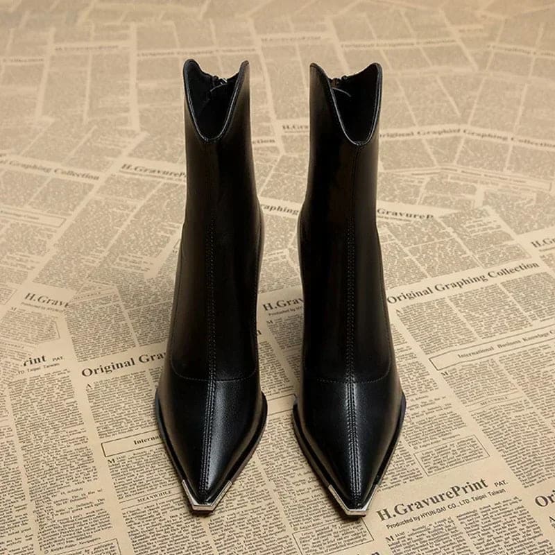 Pair of pointed toe chelsea boots with chrome tip detail and chunky block heel displayed on newspaper background_2