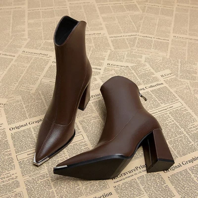 Pair of pointed toe chelsea boots with chrome tip detail and chunky block heel displayed on newspaper background_3
