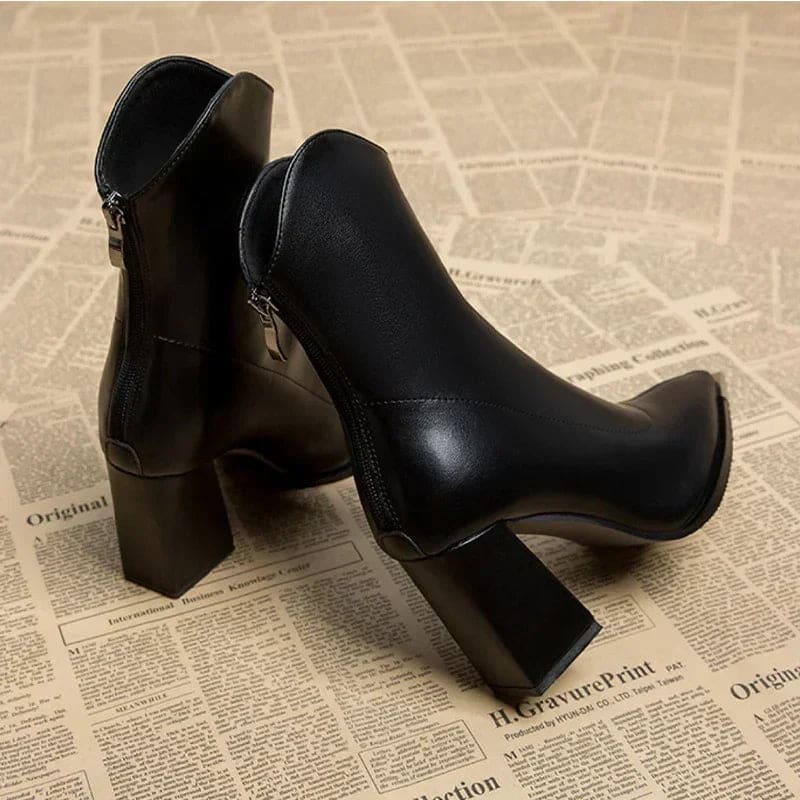 Pair of pointed toe chelsea boots with chrome tip detail and chunky block heel displayed on newspaper background_5