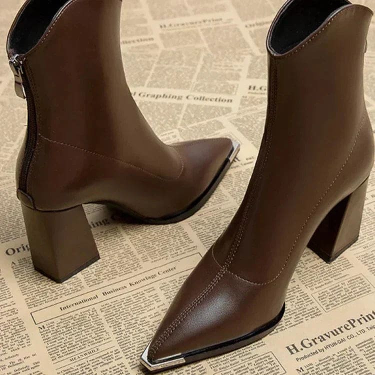 Pair of pointed toe chelsea boots with chrome tip detail and chunky block heel displayed on newspaper background_6