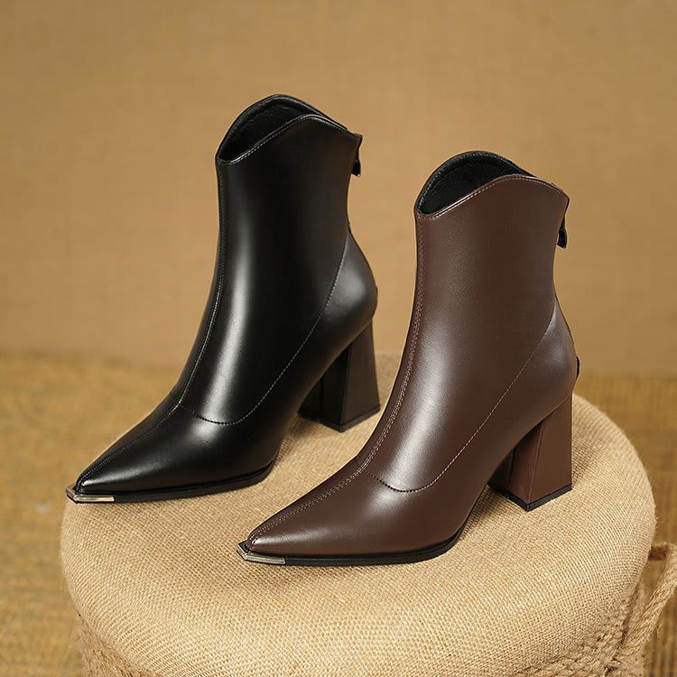 Pair of pointed toe chelsea boots with chrome tip detail and chunky block heel displayed on newspaper background_7