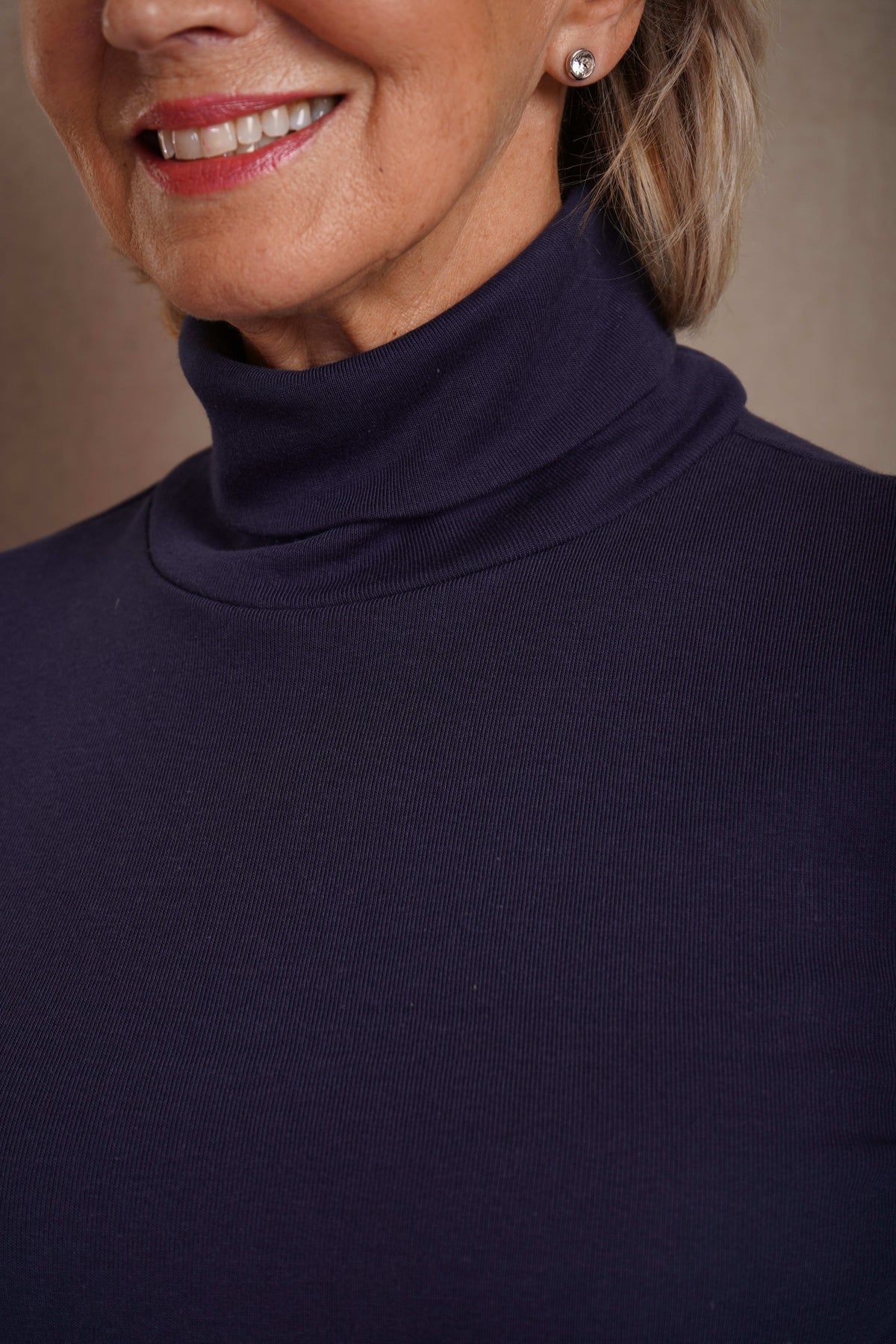 Woman wearing a beige long sleeve turtleneck top with buttoned cuffs and blue jeans against an olive backdrop._3