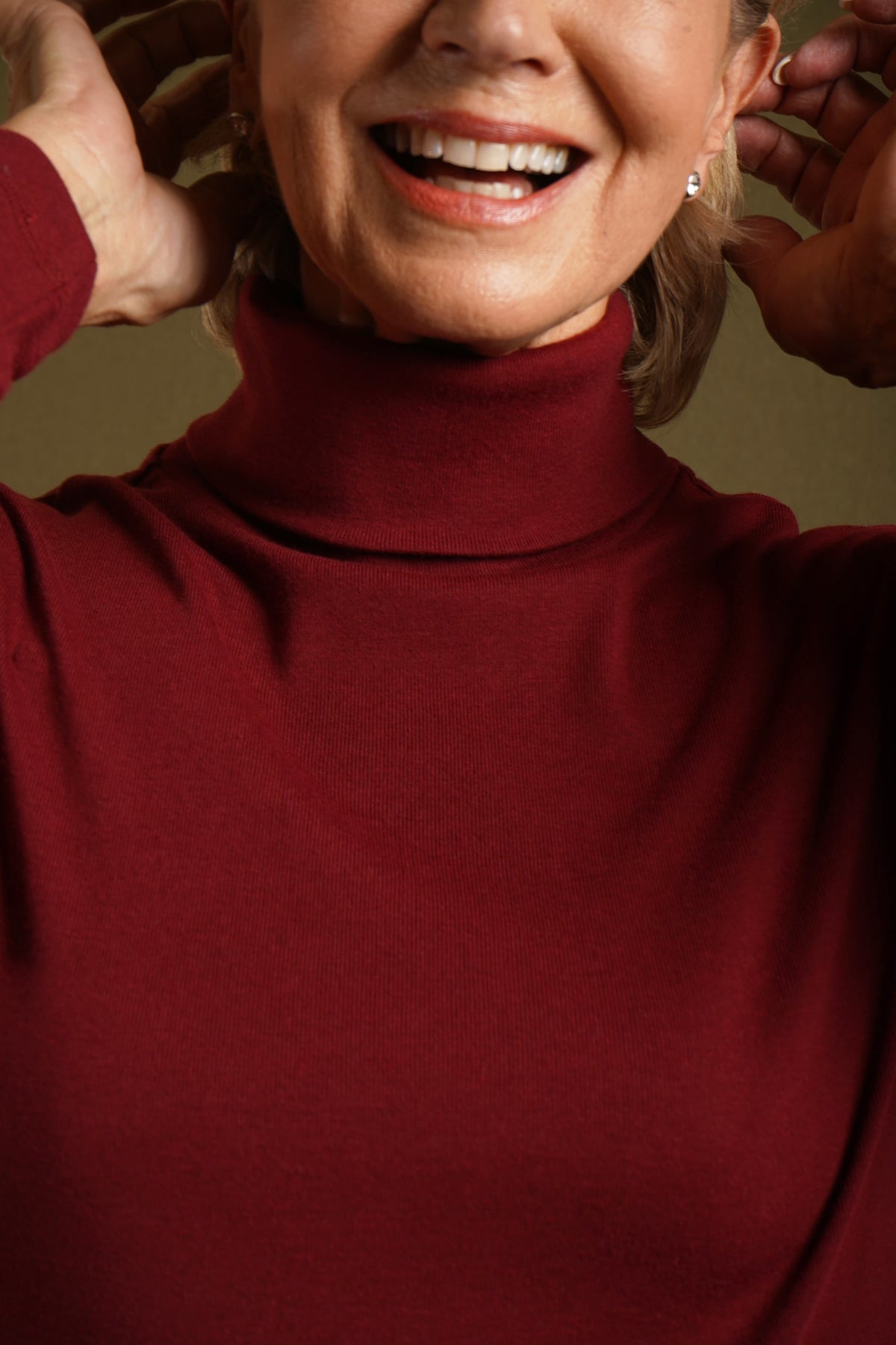 Woman wearing a beige long sleeve turtleneck top with buttoned cuffs and blue jeans against an olive backdrop._5