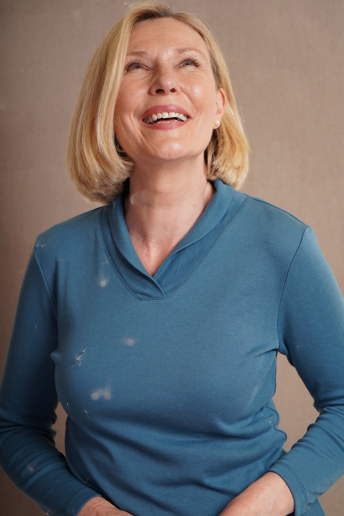 Woman with a blonde bob sitting and smiling, wearing an olive green long sleeve v-neck top with ribbed cuffs and a dark brown skirt._5